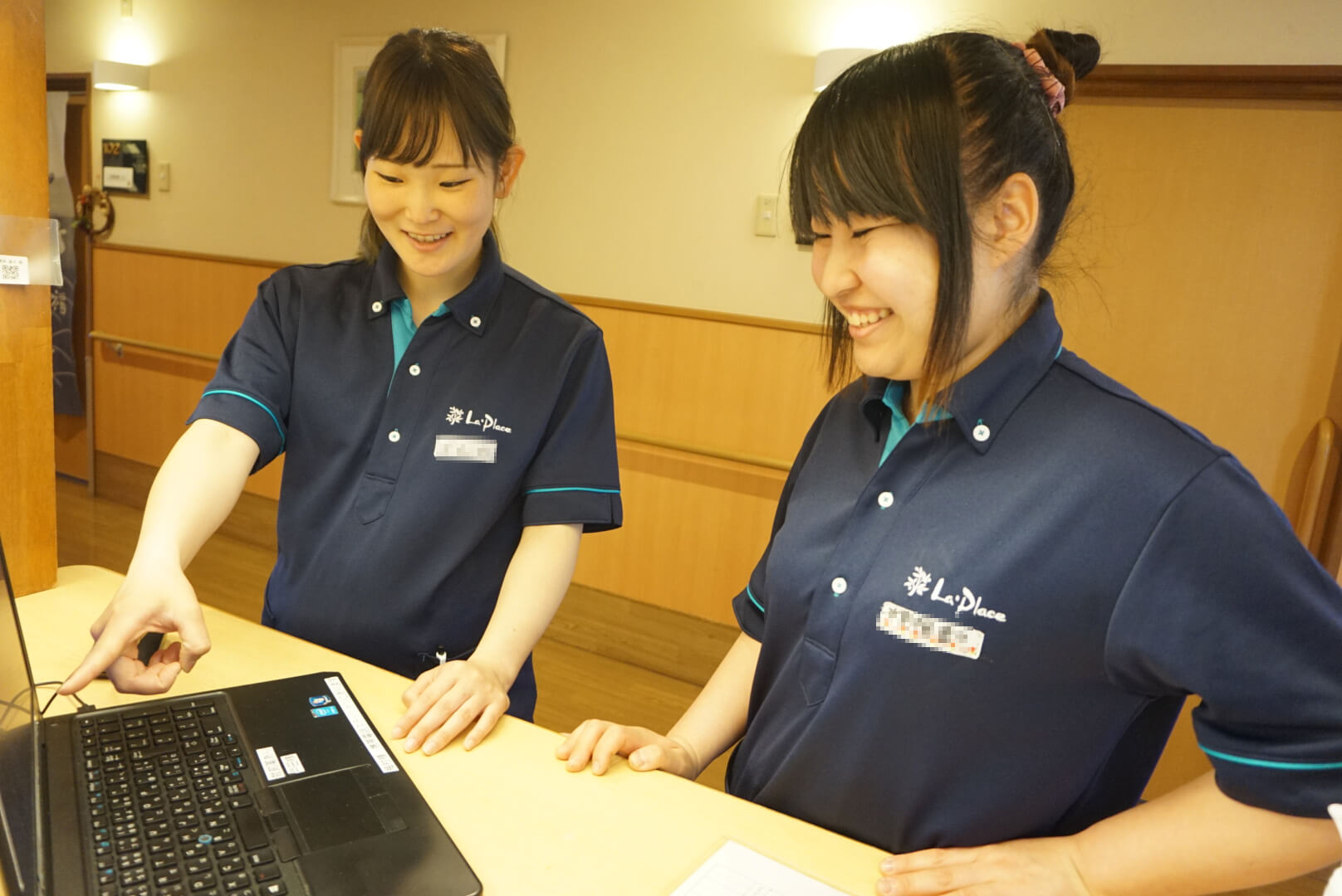 アサヒサンクリーンの女性社員２人が笑顔で話し合いながら事務作業をしている写真